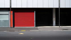 Persiana enrollable de seguridad roja e instalación de puertas automáticas en Huelva para cerramientos de clínicas y fachadas comerciales.